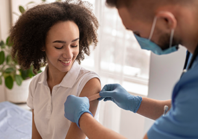 Imagem de uma mulher sorrindo, e enfermeiro colocando band-aid no braço dela